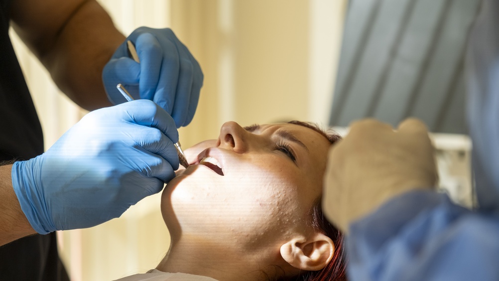 Close up of a patient smiling, revealing a full set of gleaming white dental implants, with a dentist in the background checking the alignment. No text on image.